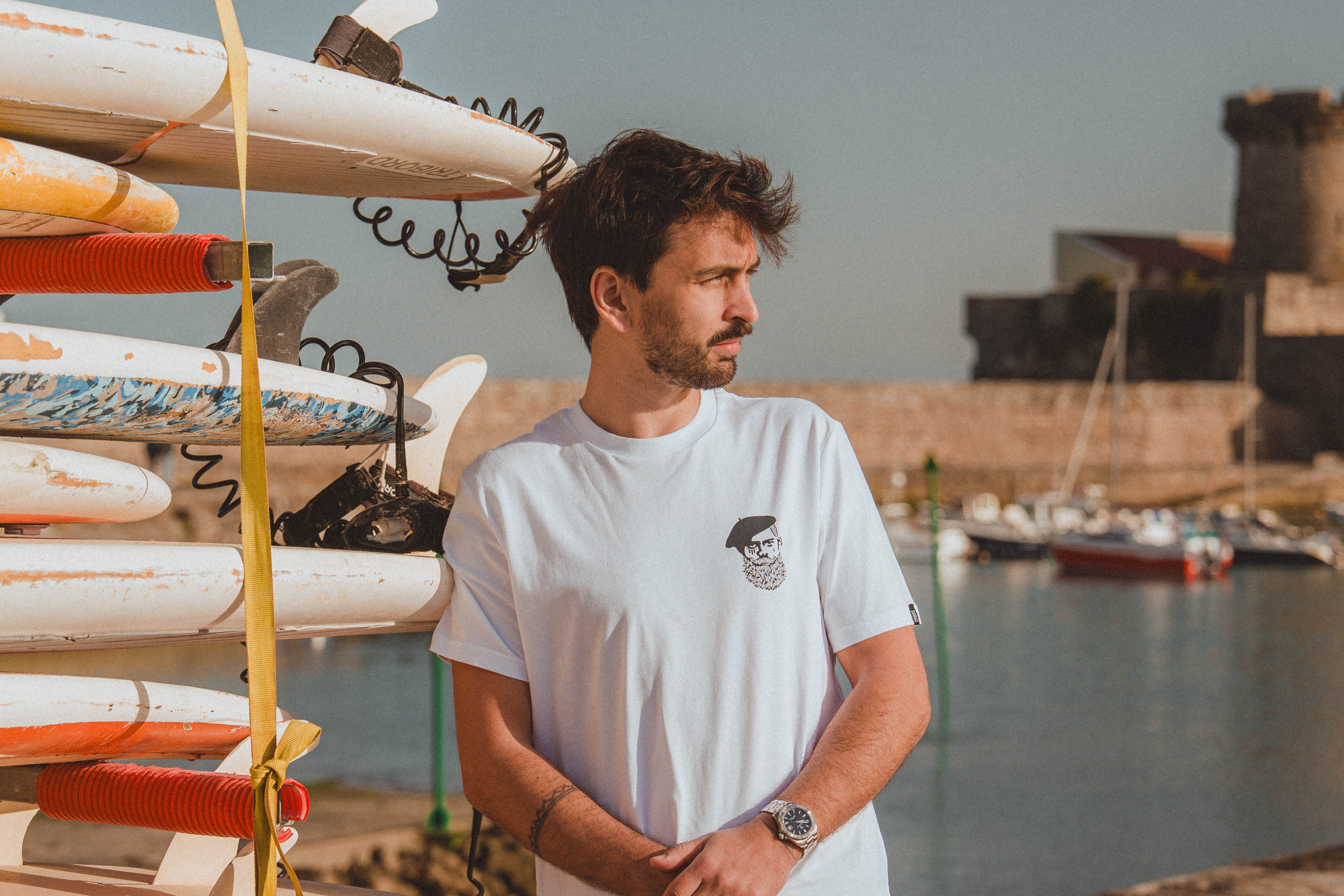 Homme en tee-shirt basque blanc Katxi Klothing devant un rack de planches de surf