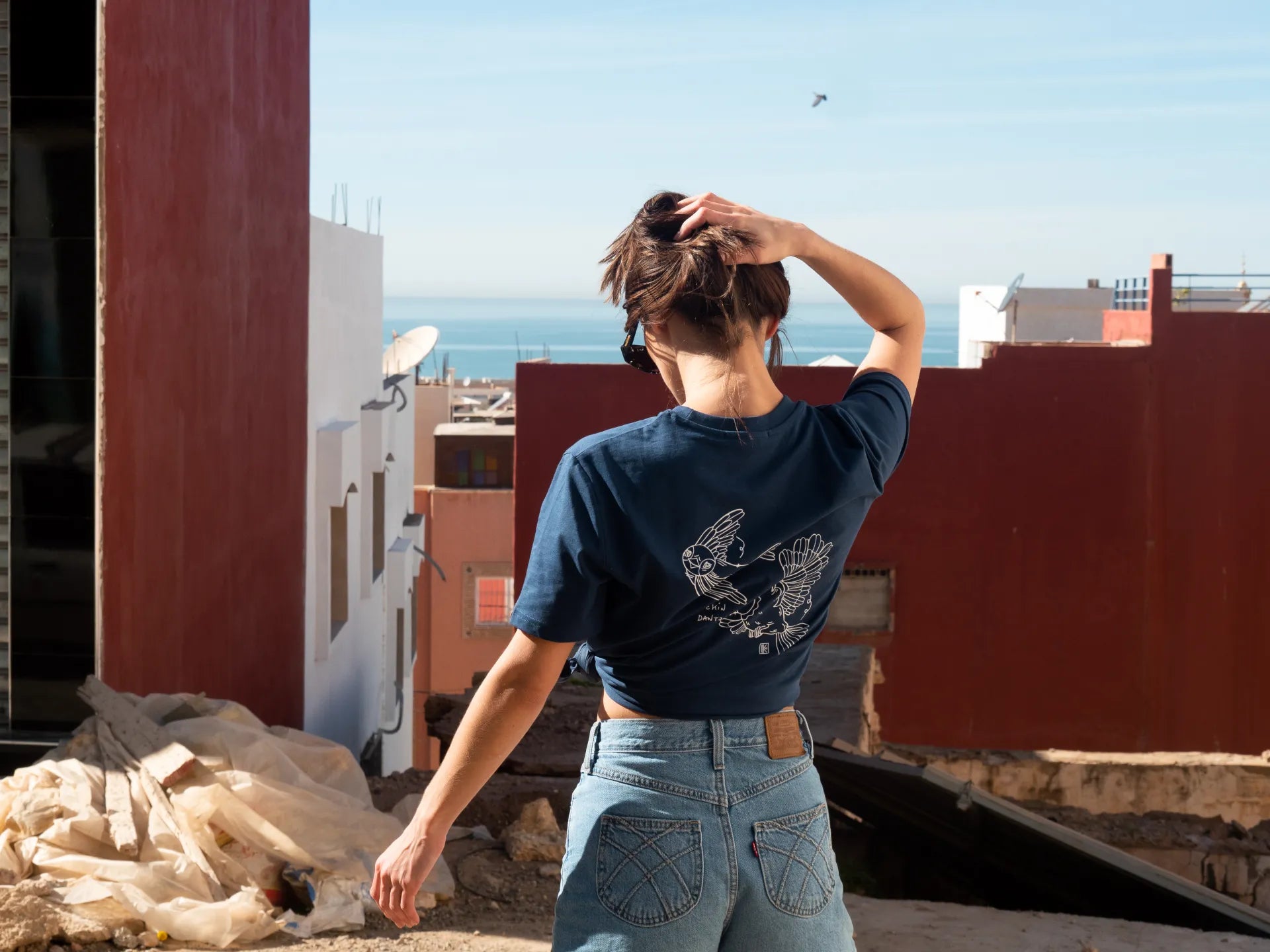 Femme de dos en tee-shirt marine Txoriak Katxi Klothing, village face à l'océan