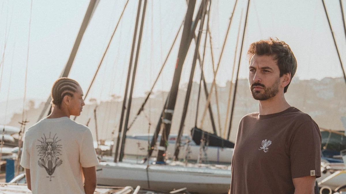 Deux hommes en tee-shirts basques Katxi Klothing écru et marron sur un port de voiliers du Pays basque